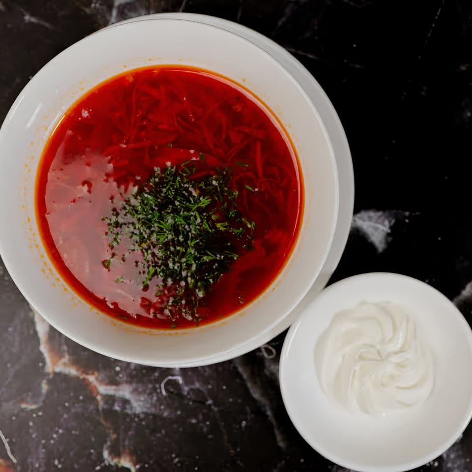Halal borscht soup with dill and a side of sour cream on a dark marble table.