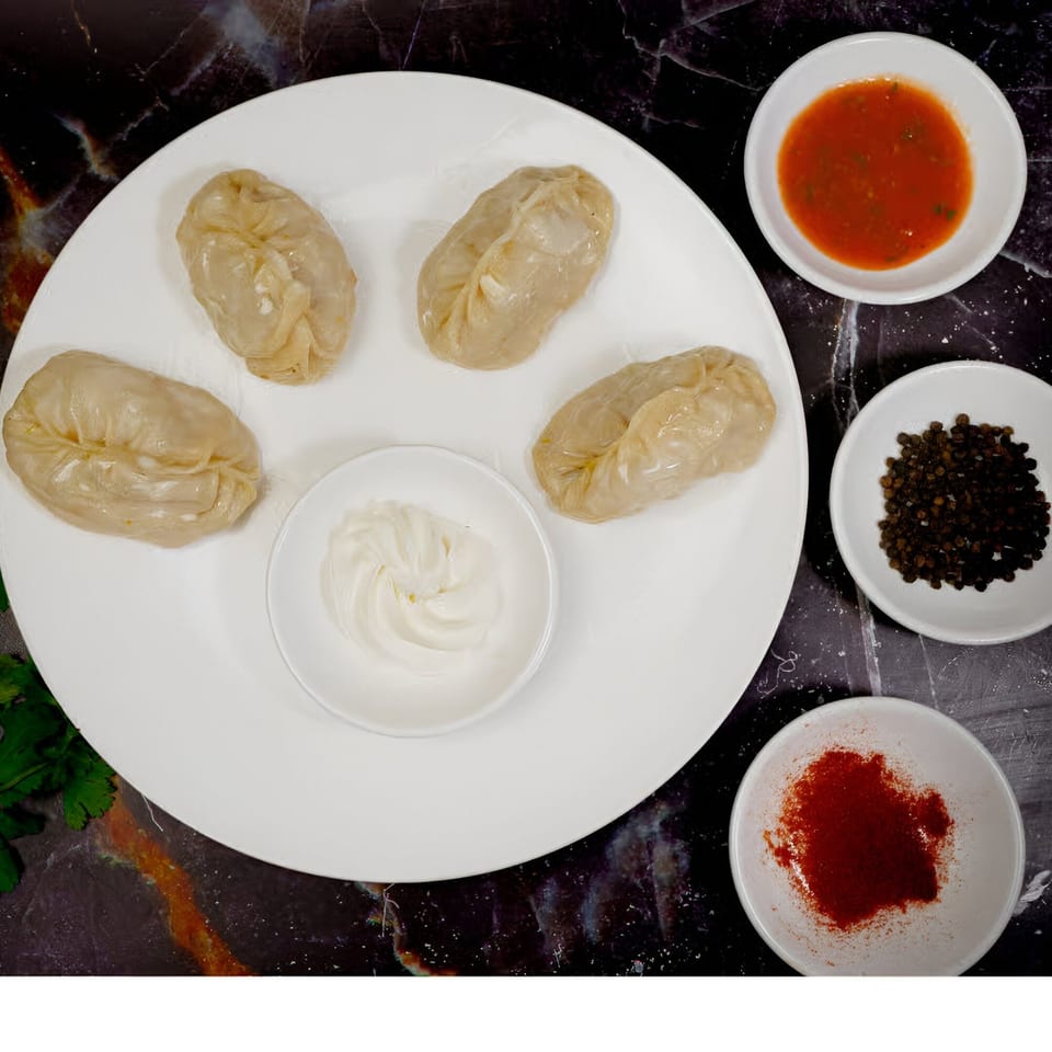 Five halal dumplings with red sauce, white sauce, black peppercorns, and red pepper flakes.