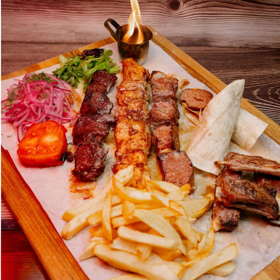 Karavan Grill's halal platter with three skewers of meat, fries, salad, tomato, and flatbread, with a flaming cup.
