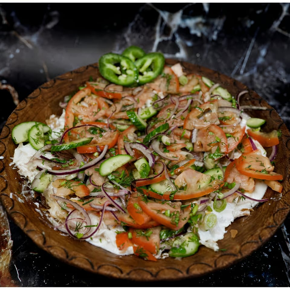 Halal salad with sliced tomatoes, cucumbers, red onions, and dill on a wooden plate.