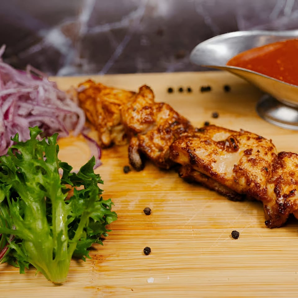 Halal chicken shish kebab on a wooden board with red sauce, sliced onions, and lettuce.